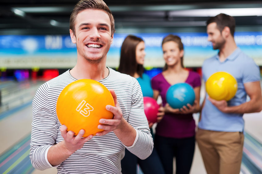 The best player. Handsome young men holding a bowling ball while three people communicating against bowling alleys